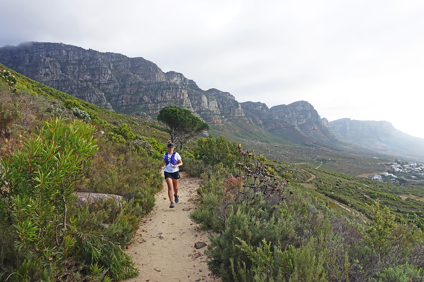 Weibliche Trailrunnerin auf dem Wanderweg Pipe Track in Kapstadt mit den 12 Aposteln im Hintergrund